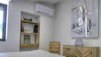 Een slaapkamer met een bed, een houten nachtkastje, een boekenkast en een wandairconditioner.