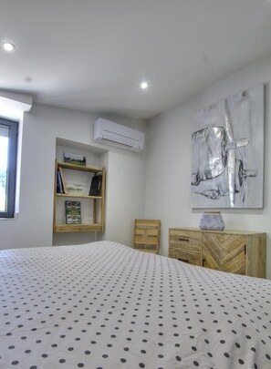 Une chambre à coucher comprenant un lit, une table de chevet en bois, une bibliothèque et un climatiseur fixé au mur.