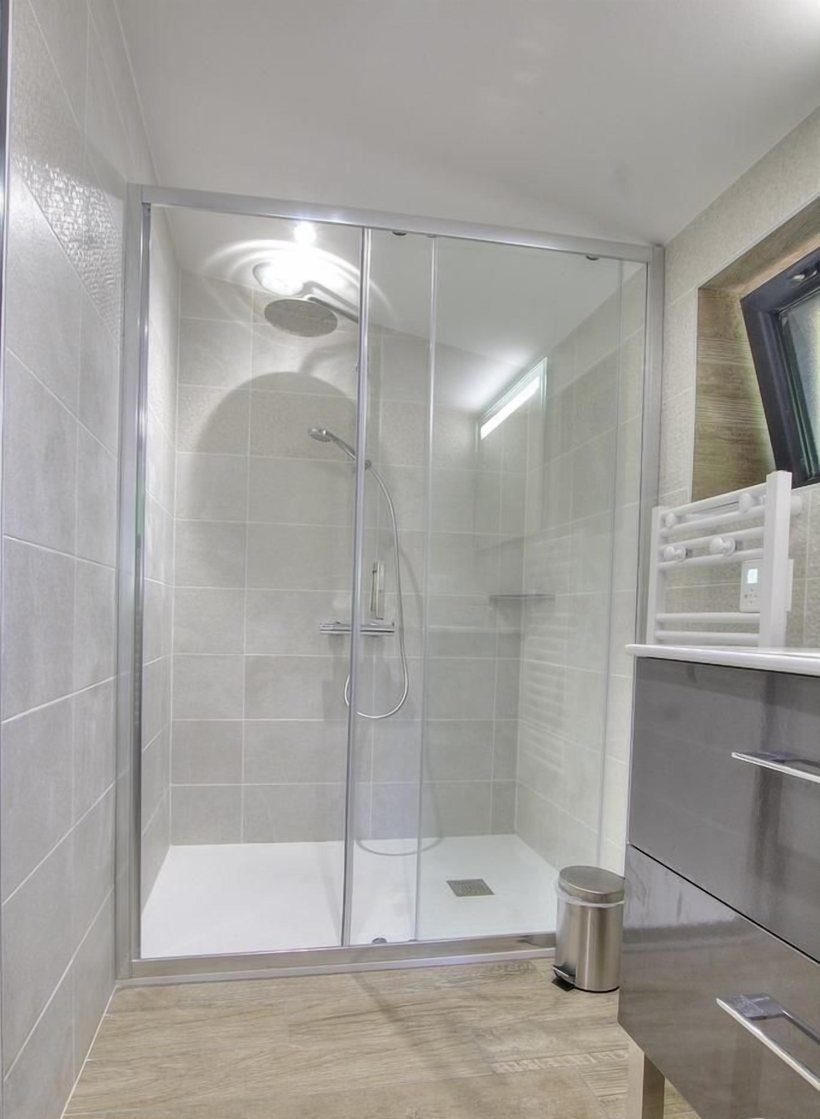 Une salle de bain moderne avec une douche à parois de verre, un évier en acier inoxydable et un plancher en bois.