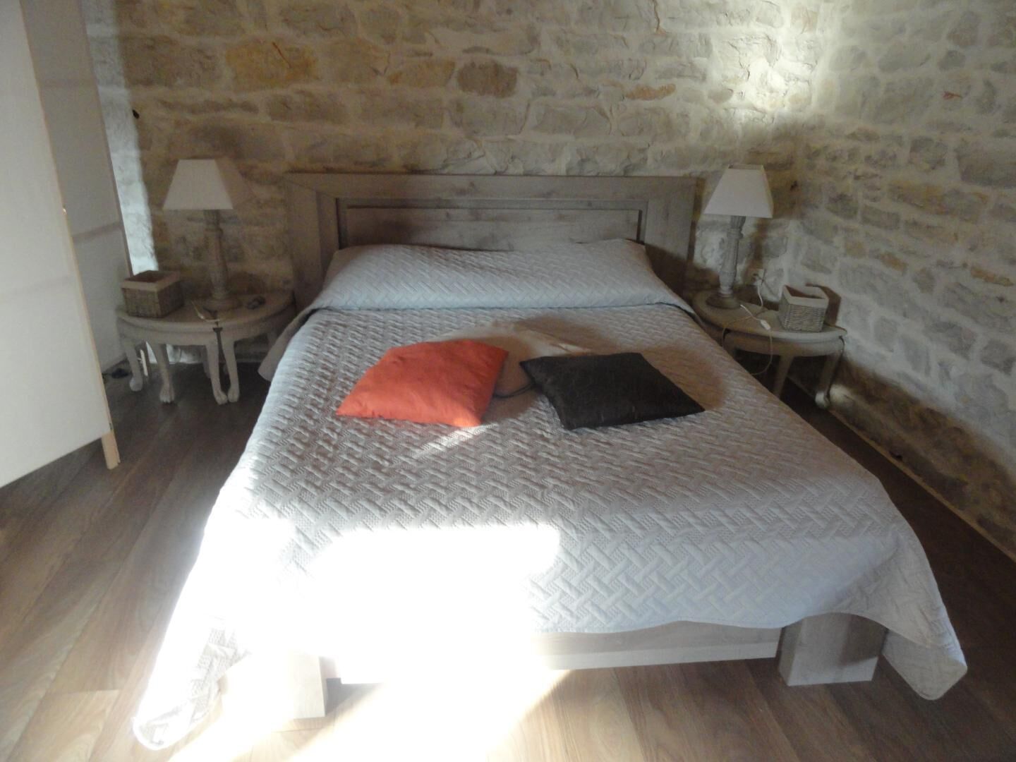 A room with a stone wall, a bed with a white bedspread, two pillows, and two bedside lamps on wooden nightstands.