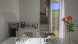 A dining area with a table set for four, a kitchen in the background, and a view of a garden through a glass door. - la Mine - Saint-martin-du-fresne (SAINT-MARTIN-DU-FRESNE)