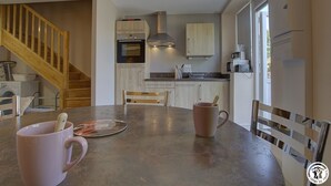 Een moderne keuken met houten kastjes, een inbouwoven en een magnetron. Er staat een eettafel met stoelen en een roze mok.