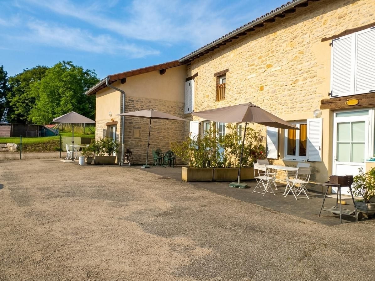 Un bâtiment doté d’une façade en pierre, d’un espace extérieur aménagé avec des tables et des chaises, et d’une cour intérieure recouverte de gravier.