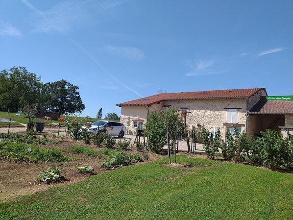A building with a stone facade and a red-tiled roof, surrounded by a well-maintained garden and a parked car. - Bugey - Tossiat - Gîte (TOSSIAT)