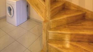 Een houten trap met een leuning, leidend naar een verdieping. Een witte wasmachine is zichtbaar op de verdieping beneden.