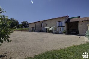 A building with a gravel driveway and a covered outdoor seating area. - Bugey - Tossiat - Gîte (TOSSIAT)