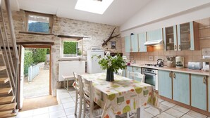 A kitchen with a dining area, a staircase, and a view of the garden. - Le Tilleul - Courmangoux (COURMANGOUX)