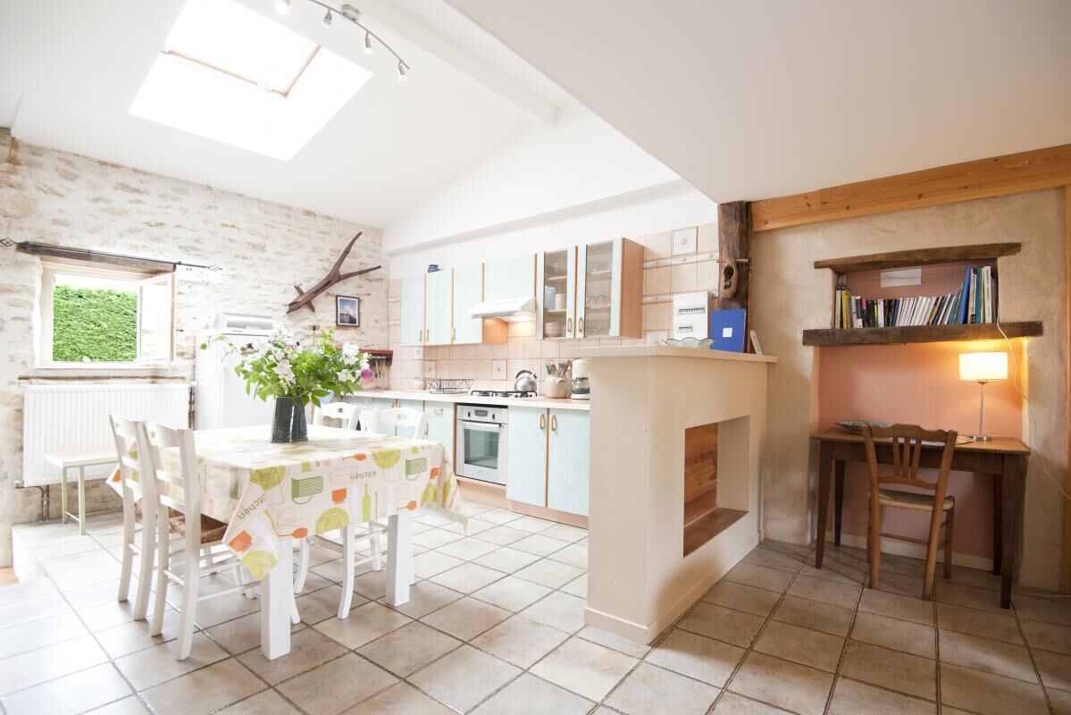 A kitchen with a dining area, featuring a table with chairs, a plant, and a bookshelf.