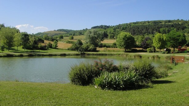A serene lakeside setting with a grassy foreground, a pond, and rolling hills in the background. - Le Tilleul - Courmangoux (COURMANGOUX)