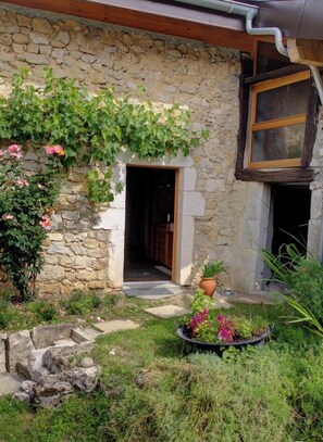 Ein Steinhaus mit einer Holztür und einem kleinen Garten mit Topfpflanzen und einer Steinsitzbank.