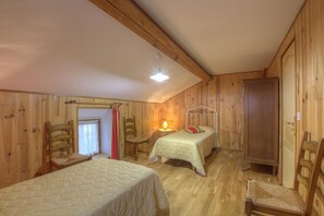Een gezellige houten kamer met twee bedden, een stoel, een kledingkast en een kleine tafel met een lamp.