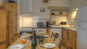 Une cuisine compacte avec des meubles en bois, une table à manger pour quatre personnes, un four à micro-ondes, une bouilloire et un réfrigérateur.