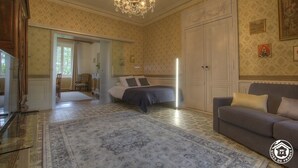 A spacious bedroom with a large bed, a sitting area with a sofa, and a chandelier.