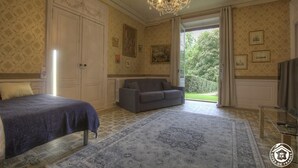 A bedroom with a bed, a sofa, a chandelier, and a view of the garden.