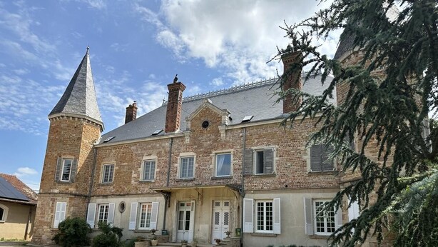 A large stone building with a prominent tower, multiple windows, and a well-maintained front garden.