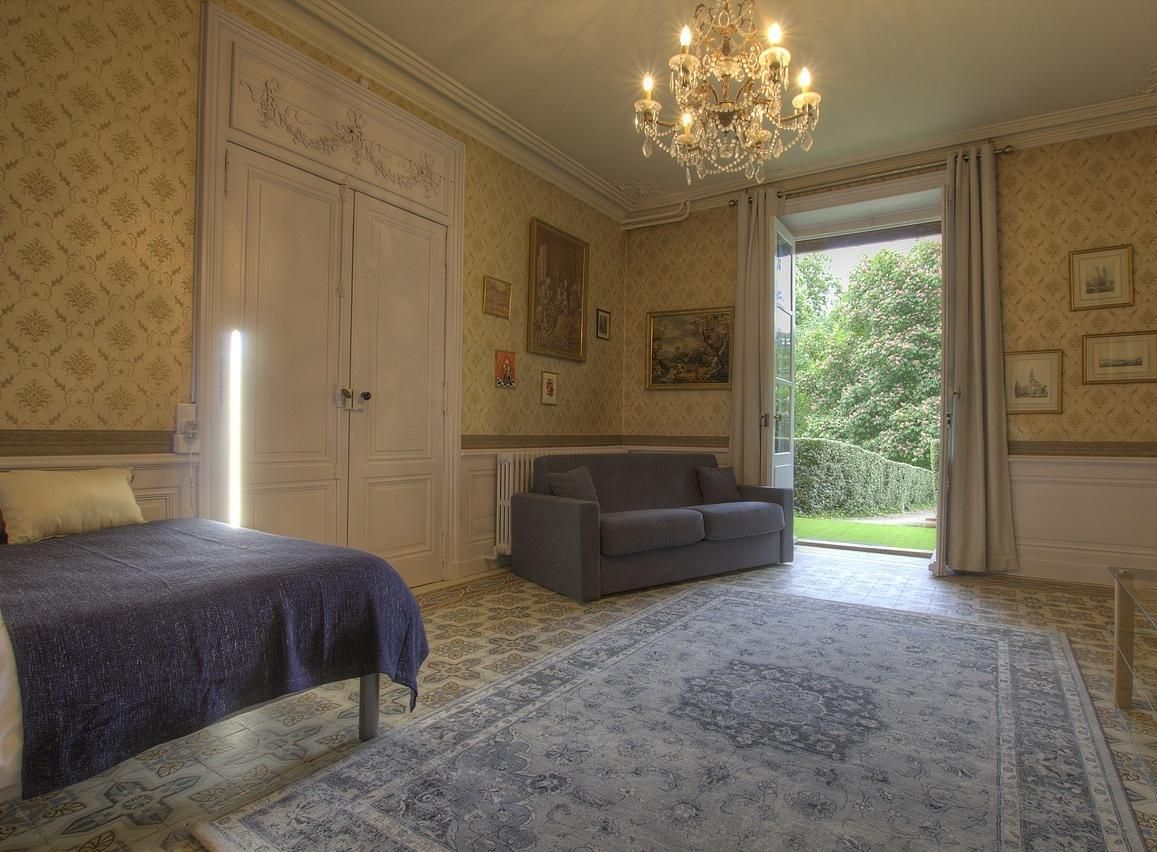 Un dormitorio con cama, sofá, candelabro y vistas al jardín.