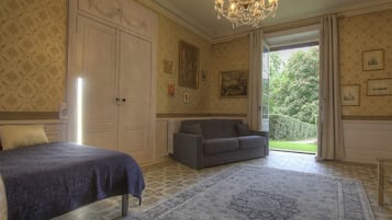 Un dormitorio con cama, sofá, candelabro y vistas al jardín.