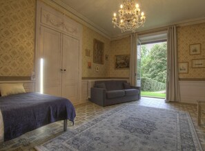 Une chambre avec un lit, un canapé, un lustre et une vue sur le jardin.