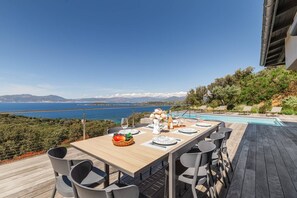 Een terras buiten met uitzicht op zee en bergen, een zwembad en een houten terras.