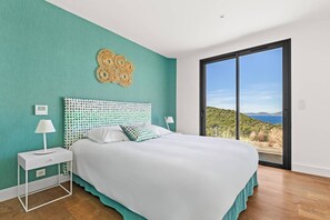 Een slaapkamer met een bed, twee nachtkastjes, een wandlamp en een groot raam met uitzicht op het landschap.