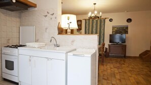 A compact kitchen with a stove, sink, and washing machine. There is a television and a decorative lamp on a shelf. - G424020 - Tramoyes - Gîte (TRAMOYES)
