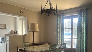 A dining area with a table set for four, a chandelier, and a view through a window with curtains. - G424020 - Tramoyes - Gîte (TRAMOYES)
