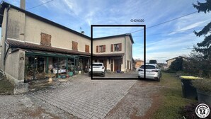 A two-story house with a tiled roof, a visible chimney, and a paved driveway. - G424020 - Tramoyes - Gîte (TRAMOYES)