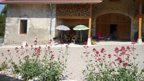 Un bâtiment en pierre avec un toit en tuiles, des tables à l’extérieur sous des parasols et une allée gravillonnée.