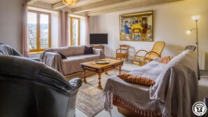 Un salon confortable avec un canapé, un fauteuil et une table basse. Un tableau est accroché au mur et un téléviseur est posé sur un meuble.