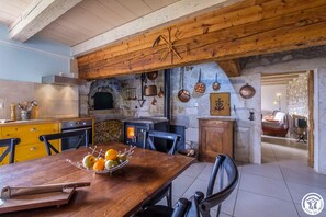 Een rustieke keuken met een stenen muur, houten balken en diverse keukengerei aan de wand.