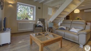En rummelig stue med stort vindue, sofa, sofabord og trappe.
