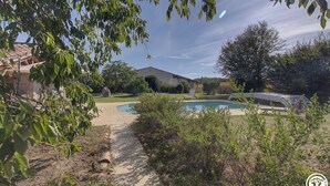 En baghave med swimmingpool, overdækket terrasse og et hus.
