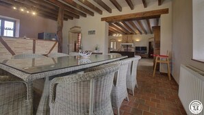 Un comedor con una mesa de vidrio rodeada de sillas de mimbre, vigas de madera en el techo y piso de ladrillo.