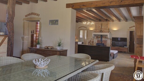 Amplia sala de estar con mesa de comedor de vidrio, mobiliario de mimbre, chimenea y televisor.