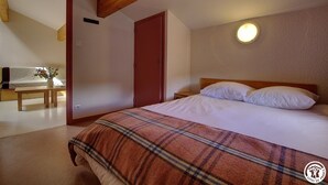 A bedroom with a bed, a bedside table, a bench, a door, and a round wall light.