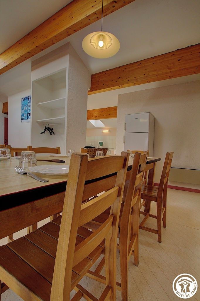 Ein Essbereich mit Holzkstühlen und einem Tisch, einer hängenden Leuchte und einem weißen Kühlschrank im Hintergrund.