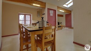 A spacious dining area with wooden tables and chairs, a large pot on the table, and a skylight above.