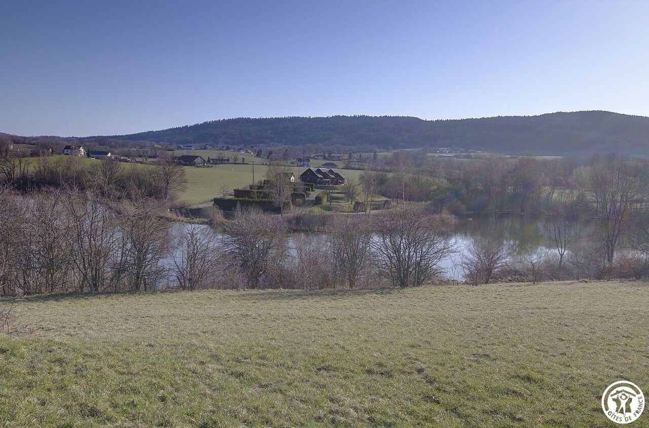 Ländliche Landschaft mit einem See, Häusern und Hügeln im Hintergrund.