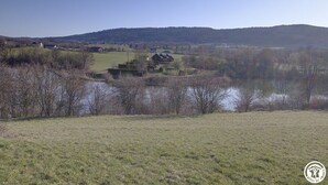 A rural landscape with a lake, houses, and hills in the background.