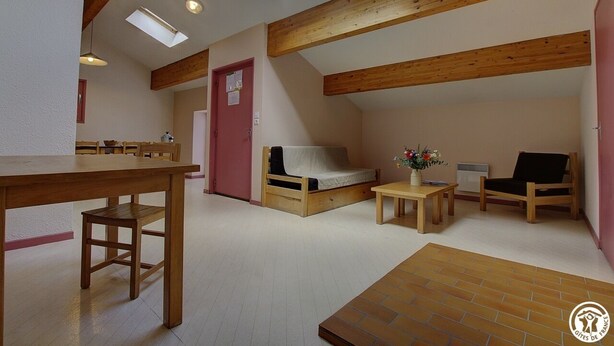 A cozy loft-style room with a wooden ceiling, a skylight, a bed, a table, and a chair.