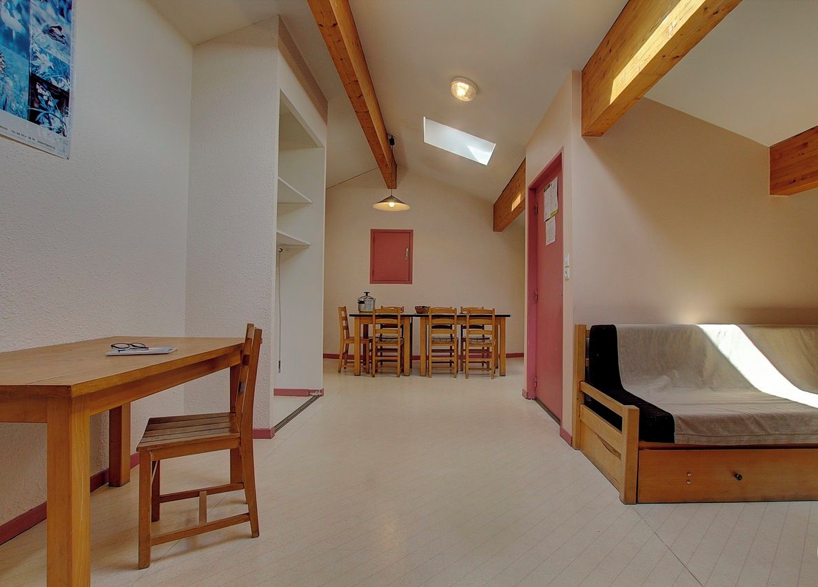 Une pièce de taille modeste comprenant un lit en bois, une table à manger avec des chaises et un petit coin cuisine.