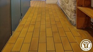 A hallway with a tiled floor, a stone wall, a blue door, and a fire extinguisher on the wall.