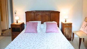 Une chambre à coucher avec une tête de lit en bois, deux lampes de chevet, une couvre-lit à motifs floraux et un fauteuil avec un coussin.