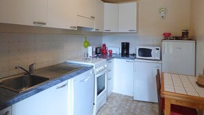 Une cuisine compacte avec des meubles blancs, un évier, une cuisinière, un four à micro-ondes et un petit réfrigérateur.