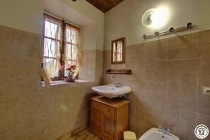 Bathroom features a sink, mirror, and shelf, with a window for natural light and a light fixture above.