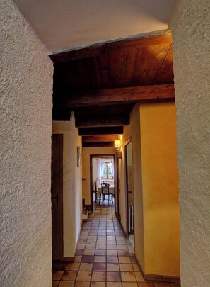 Un pasillo con suelo de baldosas, vigas de madera y una puerta a la izquierda.