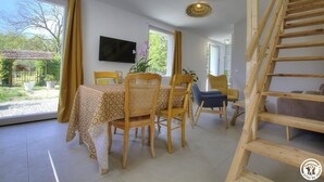 Ein Essbereich mit Tisch und Stühlen, einem an der Wand montierten Fernseher und einer Treppe rechts.