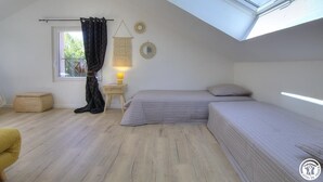 Ein kleines, gut beleuchtetes Schlafzimmer mit Dachfenster, einem Bett, einem Nachttisch mit Lampe und einem Fenster mit Vorhängen.