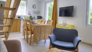 Ein gemütlicher Raum mit einer Holztreppe, einer Essecke mit Tisch und Stühlen, einem an der Wand befestigten Fernseher und einem Sofa mit einem kleinen Tisch.