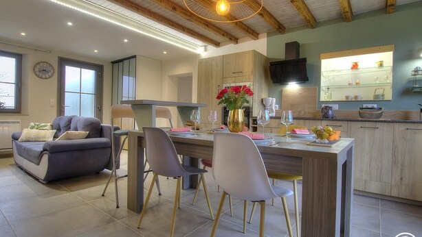 A modern kitchen with wooden cabinets, a central island, and a dining area with a sofa and chairs. - la Ferme aux Colombages (MARBOZ)
